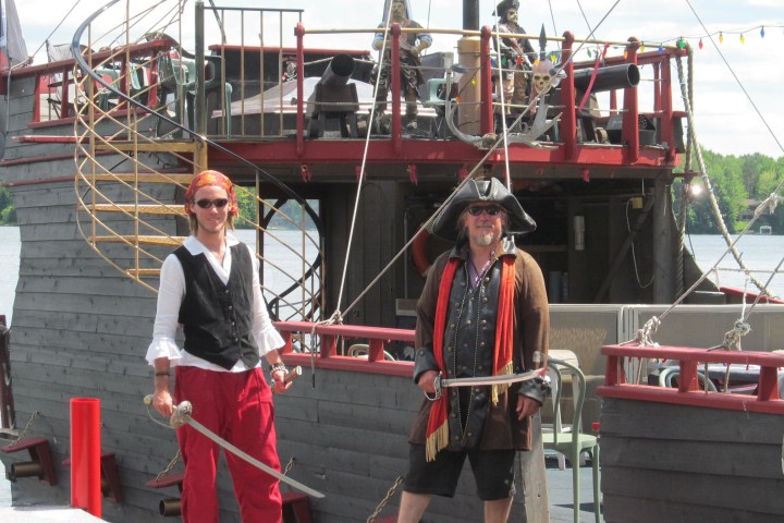 Two people in pirate costumes with a wooden ship in the background.